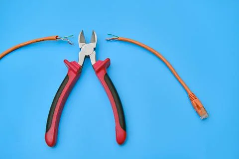 Cutting a computer network wire with wire cutters, blue studio background 写真素材
