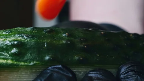 Cutting a cucumber with a knife on a red cutting board in black gloves in 4k Stock Footage 99220188