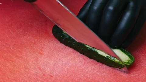Cutting a cucumber with a knife on a red cutting board in black gloves in 4k Stock Footage 99220969