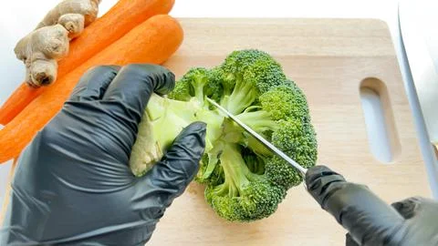 Cutting fresh broccoli florets with sharp knife on the wooden board. Stock Photos