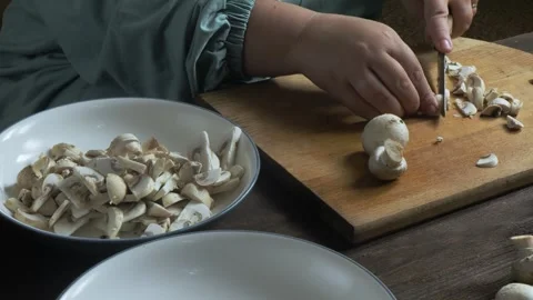 Cutting fresh champignons with a knife on a cutting board on a wooden table.. Stock Footage 332734350