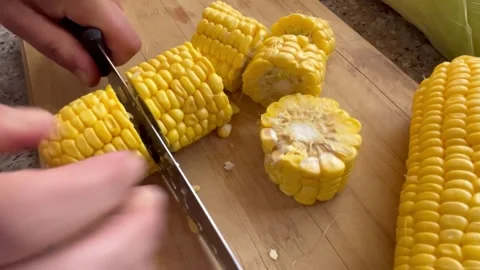 Cutting Fresh Yellow Corn Cobs on a Wooden Cutting Board Stock Footage 345320245