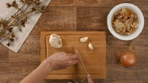 Cutting garlic on wooden kitchen table as a preparation for cooking potato soup Stock Footage 104014076
