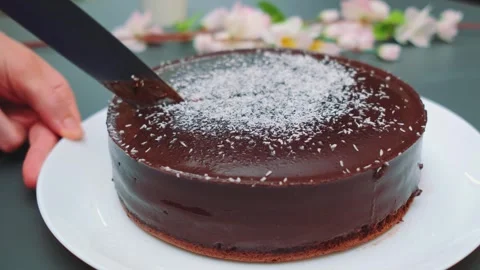 Cutting a glossy dark chocolate cake with powdered sugar indoors Stockbeeldmateriaal 342885707