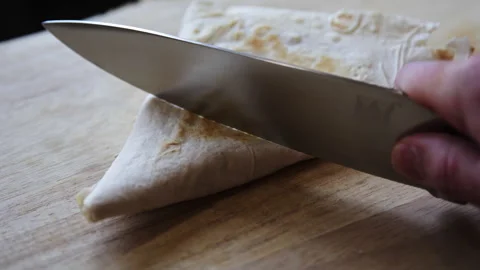 Cutting a Grilled Lavash Wrap with a Knife on a Wooden Board Stock Footage 331994144