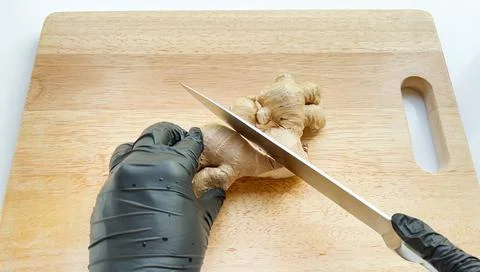 Cutting in a half of mature ginger root with a sharp knife on the wooden board. Stockfoto's