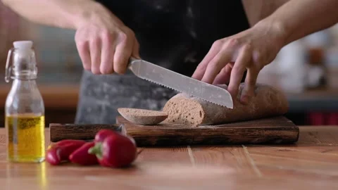 Cutting with a Knife Crusty Artisan Bread in the Kitchen on a Sunny Day. Close Stock Footage 261427603
