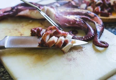Cutting octopus with knife on kitchen table. Concept of Seafood. Stock Photos