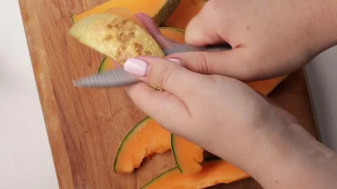 Cutting orange melon into pieces and peeling rind. Close-up of hands preparing Stock Footage 316676005