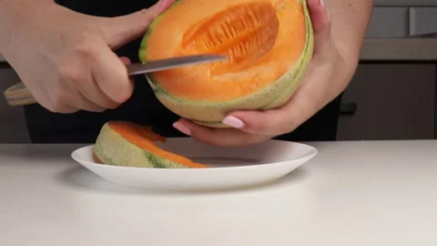 Cutting orange melon into slices on white plate. Close-up of hands preparing Stock Footage 316673078