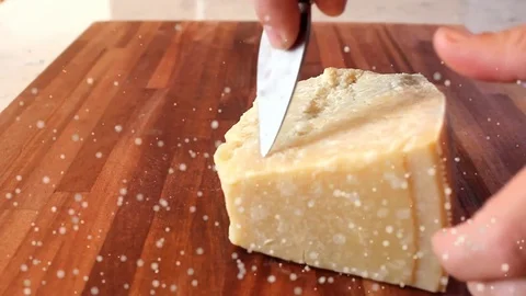 Cutting pieces of parmesan cheese with a knife on a wooden chopping board Stock Footage 69942965