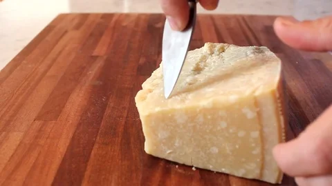 Cutting pieces of parmesan cheese with a knife on a wooden chopping board Stock Footage 69942976
