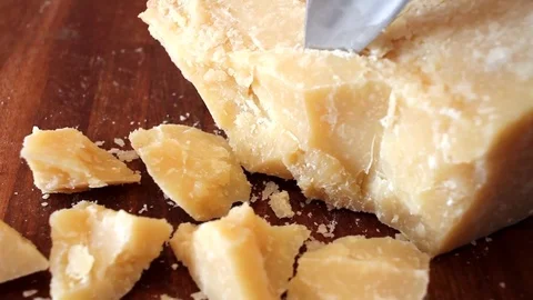 Cutting pieces of parmesan cheese with a knife on a wooden chopping board Stock Footage 69942979
