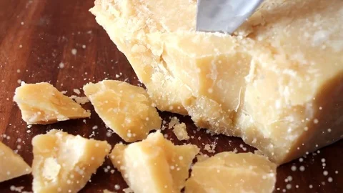 Cutting pieces of parmesan cheese with a knife on a wooden chopping board Stock Footage 69943050