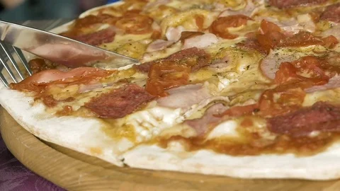 Cutting a pizza with the help of a fork and knife Stock Footage 69999065