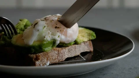 Cutting poached egg with runny egg yolk over rye bread toast with mashed avocado Stock Footage 163455075