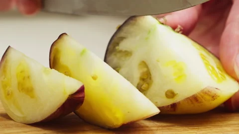 Cutting purple tomato with yellow core on wooden desk with knife close-up macro Stock Footage 256728020