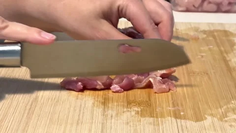 Cutting raw chicken thighs into small pieces on a wooden cutting board in the Stock Footage 315924566