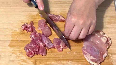 Cutting raw chicken thighs into small pieces on a wooden cutting board in the Vídeo Stock 315924583