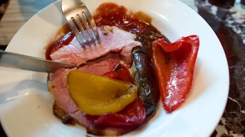 Cutting Roasted Ham Slice with Grilled Peppers on a White Plate Stock Footage 334829198
