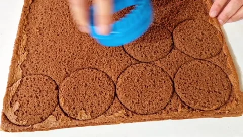 Cutting round circles from chocolate sponge cake sheet using a blue cookie cutte Stock Footage 326633534