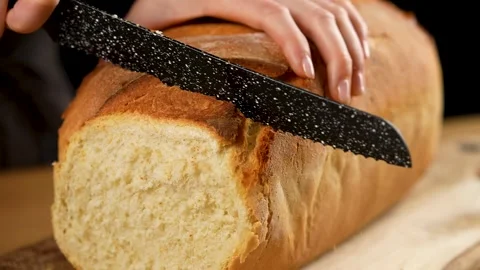 Cutting a slice of freshly baked bread with a serrated knife in slow motion 4K Stock Footage 266222696