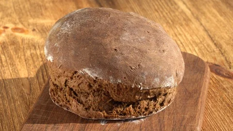 Cutting slices of rye brown bread with knife on wooden board, closeup dark bread Stock Footage 95195520