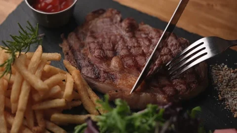 Cutting steak with knife and fork on black plate, slow motion 4k 120p Stock Footage 157992327