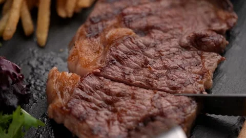 Cutting steak with knife and fork on black plate, slow motion 4k 120p Stock Footage 157992422
