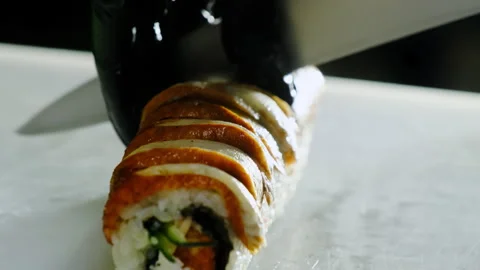 Cutting sushi roll with smoked eel with sharp knife on plate Video stock 324805349