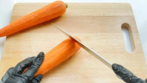 Cutting off the top of carrot with a sharp knife on the wooden board. Stock Photos