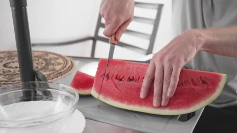 Cutting watermelon on a table with a knife in a bright kitchen setting Stock Footage 340193631