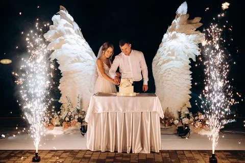 Cutting the wedding cake against the backdrop of white wings Stock Photos