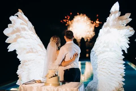Cutting the wedding cake against the backdrop of white wings Stock Photos