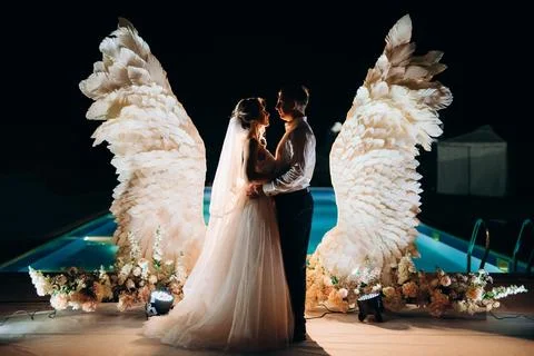 Cutting the wedding cake against the backdrop of white wings Stock Photos