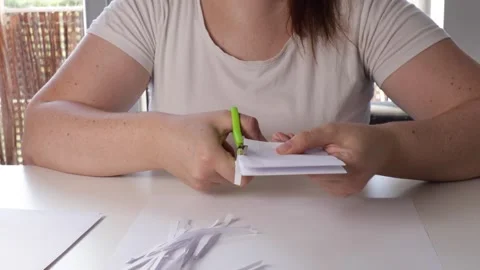 Cutting white paper into strips with scissors. Hands atwork in bright room. DIY Stock Footage 316471099