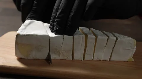 Cutting of white soft moldy Brie cheese on wooden cutting board with knife Stock Footage 305329793