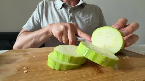 Cutting zucchini slices with kitchen knife on wooden board Stock Footage 337482141