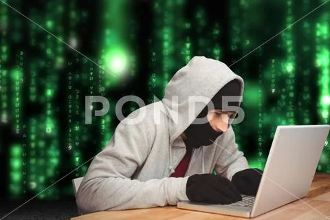 Cyber criminal hacking from a laptop on a desk against matrix code rain Stock Photos