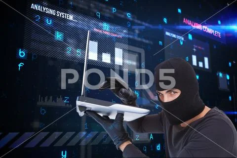 Cyber criminal holding a laptop and wearing a hood against matrix background Stock Photos