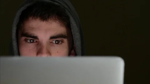 Cyber Criminal Using Laptop With Face Illuminated By Screen Stock Footage 75783160