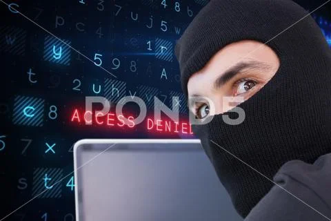 Cyber criminal wearing a hood uses a laptop against website code background Stock Photos