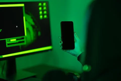 Cyber security concept showing hacker holding mobile phone in dark room Stock Photos