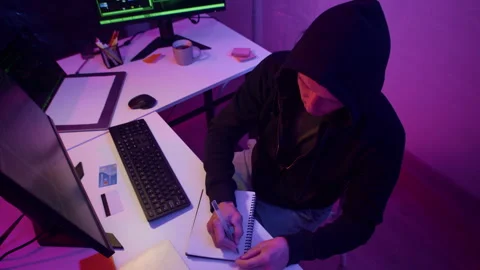 Cybercriminal Taking Notes while Coding on Computer in Neon Room Stockbeeldmateriaal 303561119