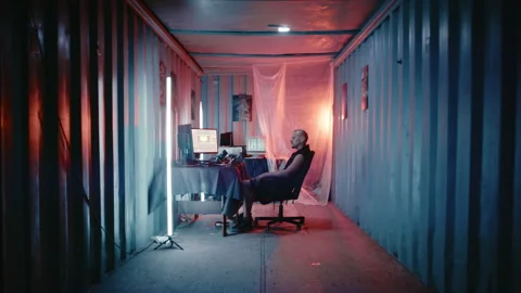 Cyberpunk hacker working on computers in a dark shipping container Stock Footage 341656413
