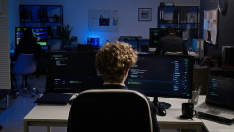 Cybersecurity Analyst Working on Dual Monitors in Modern Office Stock Footage 347296076