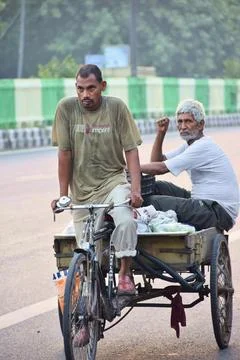 Cycle rickshaw worker transporting passenger on city road Stock Photos