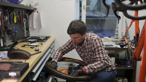 Cycle technician fitting new tire and tube to wheel of road bike. Workstation Stock Footage 270537272