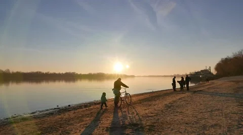 Cyclist and child are walking on the river bank at sundown Stock Footage 58973653