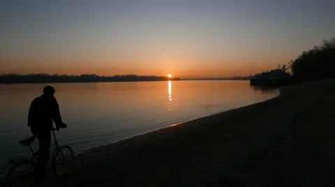 Cyclist and man on the beach of the river  at sundown Stock Footage 58973629